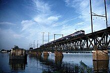 A stone bridge pier in a wide river, next to a steel truss bridge