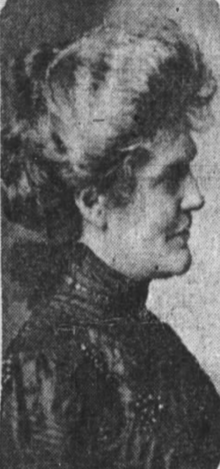 A white woman with blonde or grey hair in a bouffant updo, photographed in profile