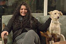 Shula Keshet sitting on a gray chair, petting her dog