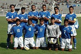 Photo of eleven men, six standing and five kneeling down, inside a stadium