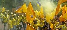 Fans in yellow shirts with yellow flags, wreathed in smoke