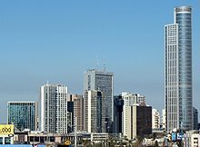 High-rise buildings in a city. A steel and glass skyscraper towers over the other buildings.