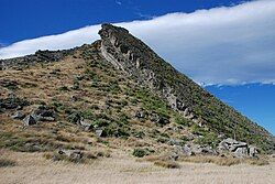 A diagonal rock face with cliffs separating it from the hillside