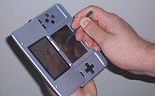 A person holds a handheld video game console in one hand and a writing tool in the other.