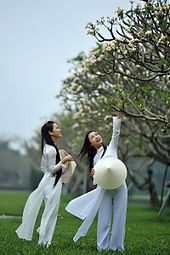 Photograph of two girls wearing a traditional Vietnamese white school uniform, the áo dài—both are holding the nón lá, a conical hat