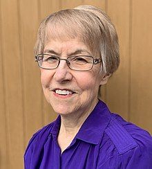 A portrait of Elizabeth Raum standing in front of a wooden door, taken in 2021.