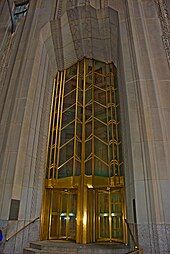 A tall arch at the entrance to 1 Wall Street. Within the arch is a bronze door frame with two sets of doors.