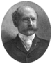 Head of a balding white man with a bushy mustache wearing pince-nez glasses and a dark suit over a light-colored shirt and tie. The portrait is framed by laurel wreaths on the bottom and the words "HON. HENRY H. BINGHAM" are below.