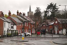 a number of buildings, mainly red, in front of a church on a hill and a row of big trees