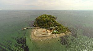 The island of Sarushima is golden on a late August day. In the lower right corner a few men on the deck of a boat look back at the island