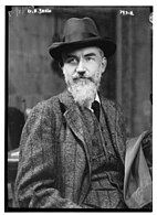 An older man with a pointy white beard wearing a tweed suit and a brimmed hat