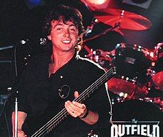 Lewis holding a bass guitar and smiling