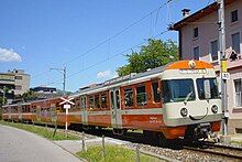 Orange three car electric trainset. The centre carriage does not match the other two and has a lower floor. The front of the train is decorated with a smile shape below the two round headlights.