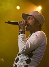 A musician wearing a white hat and a watch is singing