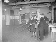 A wargame in progress. The men on the far-right command the escort ships and may only view the game board through holes in the screen. The woman in the foreground is Jean Laidlaw.