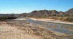 A shallow river with a sandy bed flows through an arid landscape.