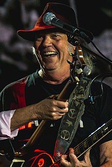 Young smiling joyously on stage, holding a guitar in each hand