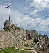 Stone tower with flag left from stone entrance.