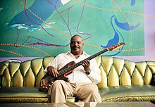 Tony Saunders sitting on a couch, holding a bass guitar