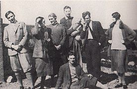 Richard Plunket Greene, first from the left, Olivia Plunket Greene, second from left, David Plunket Greene, holding the dog, Terence Lucy Greenidge, smoking, second from right, Elizabeth Frances Russell, first from the right, Evelyn Waugh, sitting down