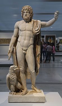 Marble statue of a bearded man, standing, with his right arm raised above his head.