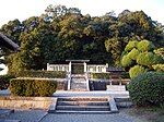 Torii gate behind a white stone fence in front of trees.