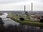 A middle-sized river flows by a factory with two tall smokestacks.