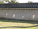 Photo of defensive loopholes in one of the castle walls. Two of the loopholes are rectangle-shaped, one is triangle-shaped, and one is circle-shaped.