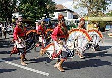 Men ride rattan horses while spectators watch