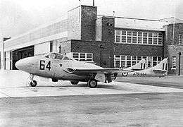 Side view of single-engined, twin-boomed military jet parked in front of a building