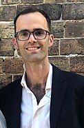 A portrait of a bespectacled man wearing a suit