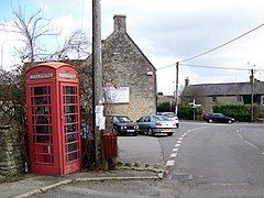 Street scene. Red telephone box and telegraph pole. Stone buildings around road junction.