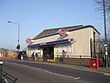 A white-bricked building with a dark blue, rectangular sign reading "LEYTON STATION" in white letters all under a blue sky fading to purple on the horizon