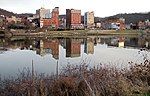 Modest skyscrapers, their images reflected in the water, line the bank of a wide placid river.