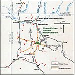 Large square map of northwestern New Mexico and neighboring parts of, clockwise from left, western Arizona, southeastern Utah, and southwestern Colorado. The map region has a green and blocky rectangular-crescent area at its center labeled "Chaco Culture National Historical Park". Radiating from the green region are seven segmented gold lines: "[p]rehistoric roads", each several dozen kilometers in length when measured according to the map scale factor. Roughly seventy red dots mark the location of "Great House[s]"; they are widely spread across the map, many of them far from the green area, near the extremes of the map, more than one hundred kilometers from the green area. Two proceed roughly south, one southwest, one northwest, one straight north, and the last to the southeast. Yellow dots mark the location of modern settlements: "Shiprock", "Cortez", "Farmington", and "Aztec" to the northwest and north; "Nageezi", "Cuba", and "Pueblo Pintado" to the northeast and east; "Grants", "Crownpoint", and "Gallup" to the south and southwest. They are connected by a network of gray lines marking various interstate and state highways. A fan of thin blue lines along the northern margins of the map depict the San Juan River and its communicants.