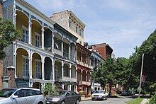 Rowhouses with arts-and-crafts styled porches (on both first and second floors) sit on a street across from a park.