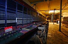 Panels of a manual telephone exchange, with plugs, wires and sockets, receding into the distance