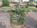 Photograph of a formal garden at the Luther Burbank House and Gardens, featuring brick walkways and planterboxes, a small lawn, a fountain and pool, low stone walls, and wooden trellises.