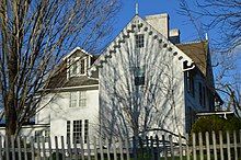 A fancy Victorian-style manor of medium size, with white-colored siding and brown asphalt shingles.