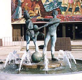 Bronze sculpture of dancing family, above burbling fountain, mosaic mural in background