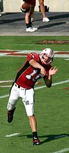 A college football quarterback throwing a football. The ball has left his hand and in the picture is a couple feet above him while he is still in the follow through motion.