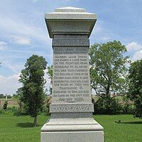 Boggs monument. Inscription reads "Capt. John Boggs born in western Penn. 1738. Married Jane Irwin and raised a large family on the frontier near Wheeling, W. Va. One son Wm. was taken prisoner by the Indians in view of his fathers cabin which is here represented. Another James was killed by them near Cambridge O. Emigrated to Ohio and built his cabin on this spot 1798 and died 1826."