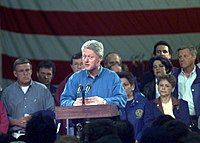 Bill Clinton is standing at a podium speaking to a crowd. The former mayor of Grand Forks is at the right of the image.