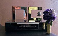 Trophy in the form of the Pesma za Evroviziju logo (Cyrillic letters P, as well as S and E combined). On the pedestal it is written "Winner of Pesma za Evroviziju – Radio and Television of Serbia 2024. There is also a bouquet of flowers in the picture