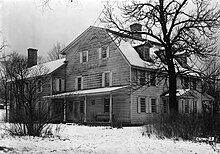 A black-and-white image of a large New England-style house with white siding