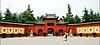 A gate with three arches, the central and largest doors being open, flanked by walls with painted chinese characters and guarded by two stone statues of lions