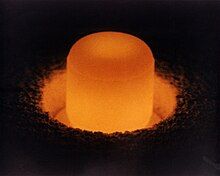 Glowing cylinder of plutonium oxide standing in a circular pit