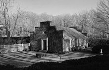 Black and white photograph of a one-storey building with one door and five windows surrounded by leafless trees.