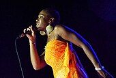 A woman wearing an orange dress while singing into a microphone.