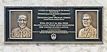 A bronze plaque that has engravings of two deceased guards at the Capitol. The text on the plaque reads: "IN HONOR AND REMEMBRANCE OF THE HEROISM DISPLAYED BY OFFICER JACOB JOSEPH CHESTNUT AND DETECTIVE JOHN MICHAEL GIBSON UNITED STATES CAPITOL POLICE WHO, ON JULY 24, 1998, HERE BRAVELY GAVE THEIR LIVES DEFENDING THE UNITED STATES CAPITOL DEDICATED BY THE HONORABLE J. DENNIS HASTERT, SPEAKER OF THE HOUSE OF REPRESENTATIVES, AND THE HONORABLE STROM THURMOND, PRESIDENT PRO TEMPORE OF THE UNITED STATES SENATE".